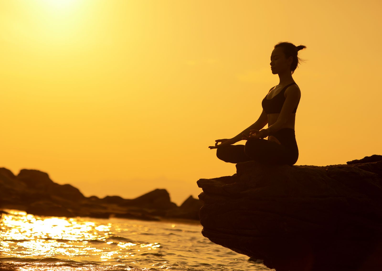 Free to use Woman practicing yoga in lotus pose on a cliff by the sea at sunset, embodying tranquility and balance.