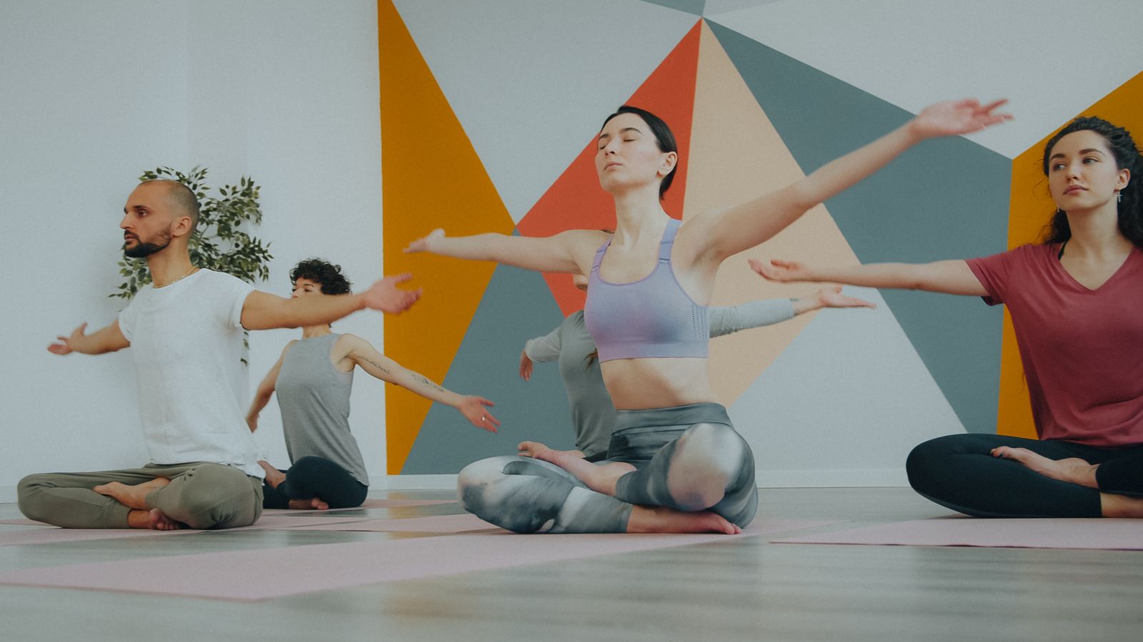 A diverse group of adults in a yoga class performing a meditative pose indoors.