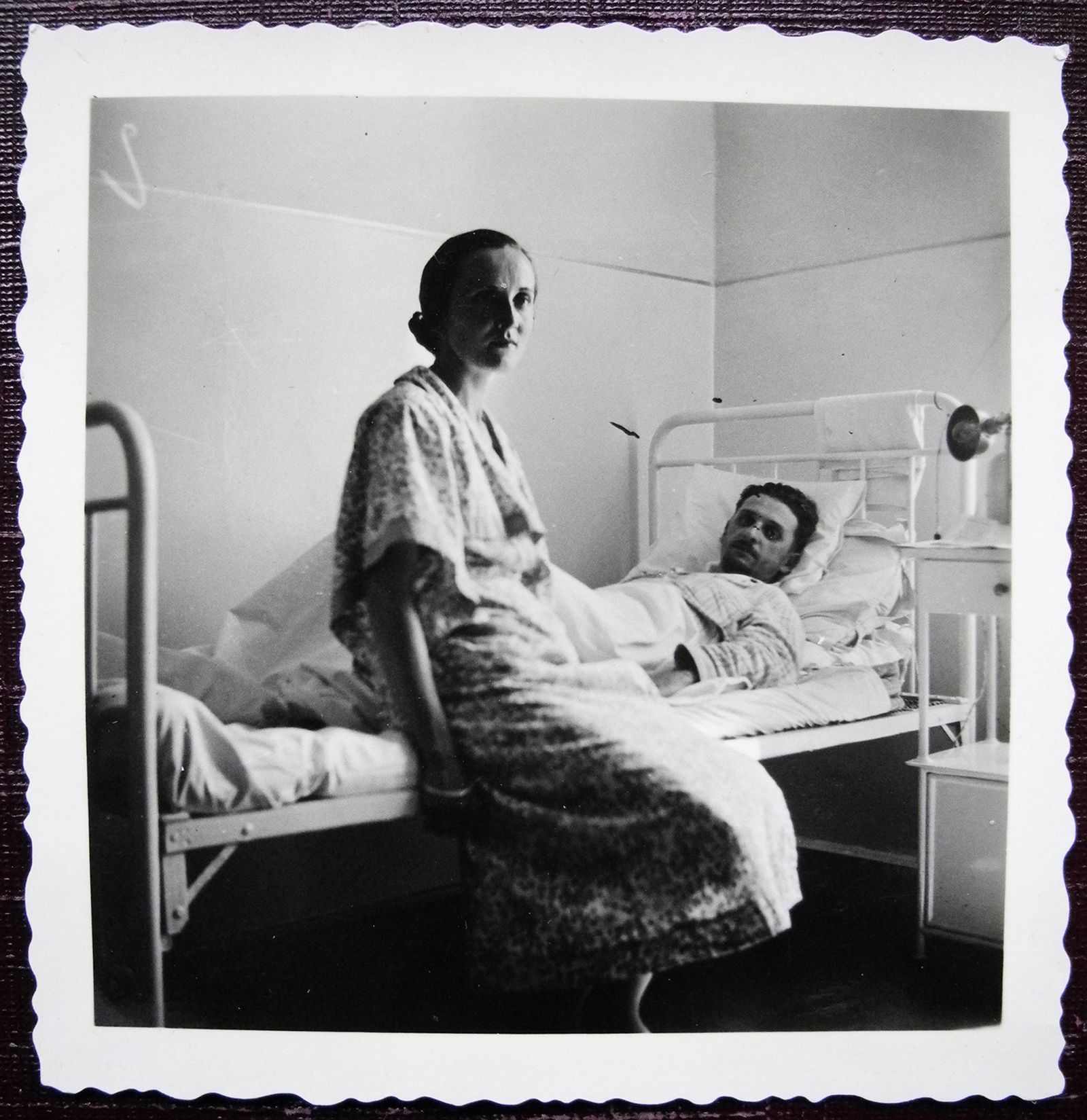Black and white photo of a woman visiting a male patient in a vintage hospital room.