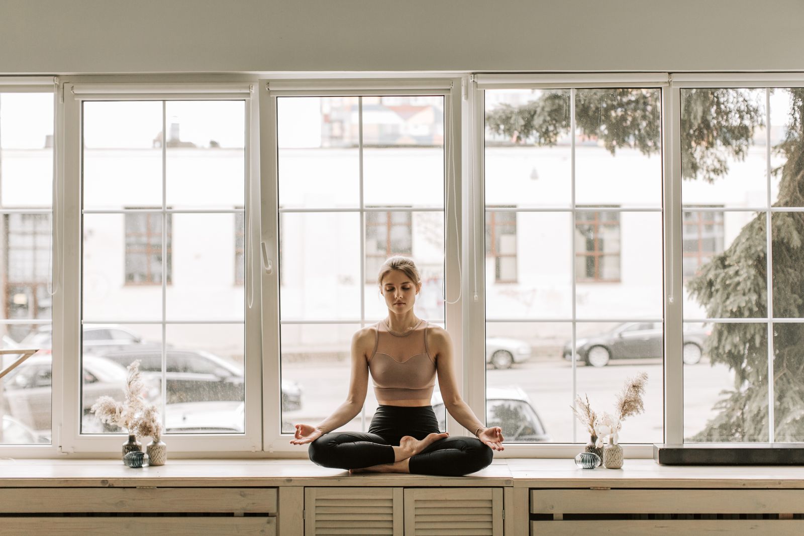 Calm woman practicing meditation on a windowsill indoors, embracing mindfulness and relaxation.