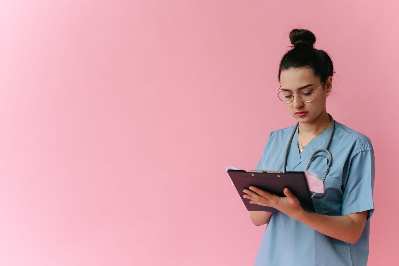 Free Professional nurse reviewing patient notes on clipboard with pink background, in studio setup.