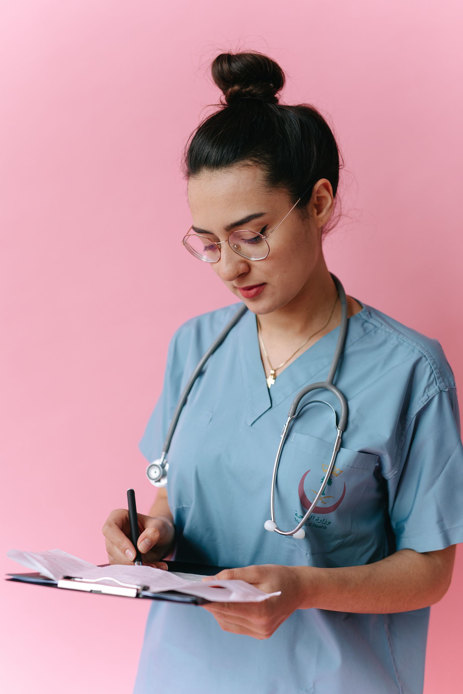 Woman in blue scrubs writing medical notes on a clipboard