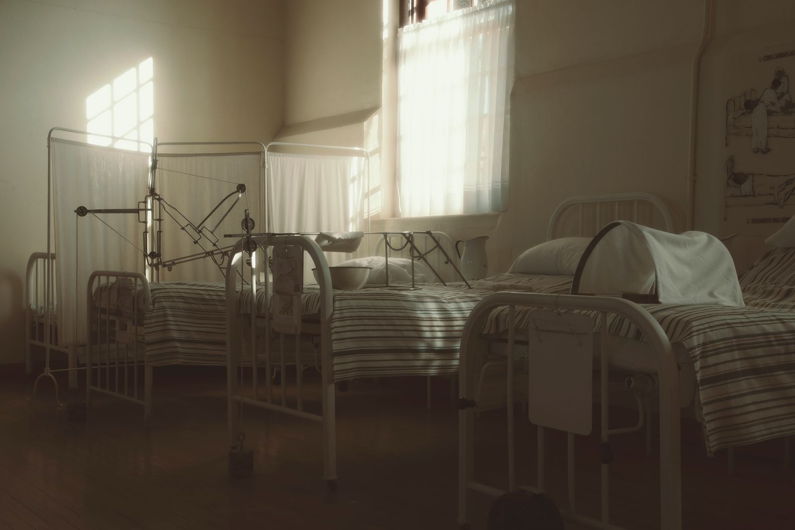 Dimly lit vintage hospital room featuring empty beds and medical equipment, creating a nostalgic atmosphere.